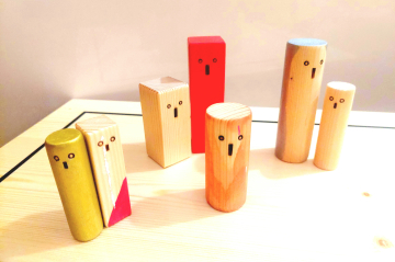 acht Holzfiguren mit aufgemaltem Gesicht sind paarweise und einzeln auf einem Tisch platziert 